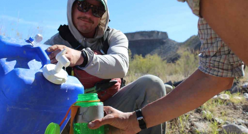 a person fills another's water bottle from a large container